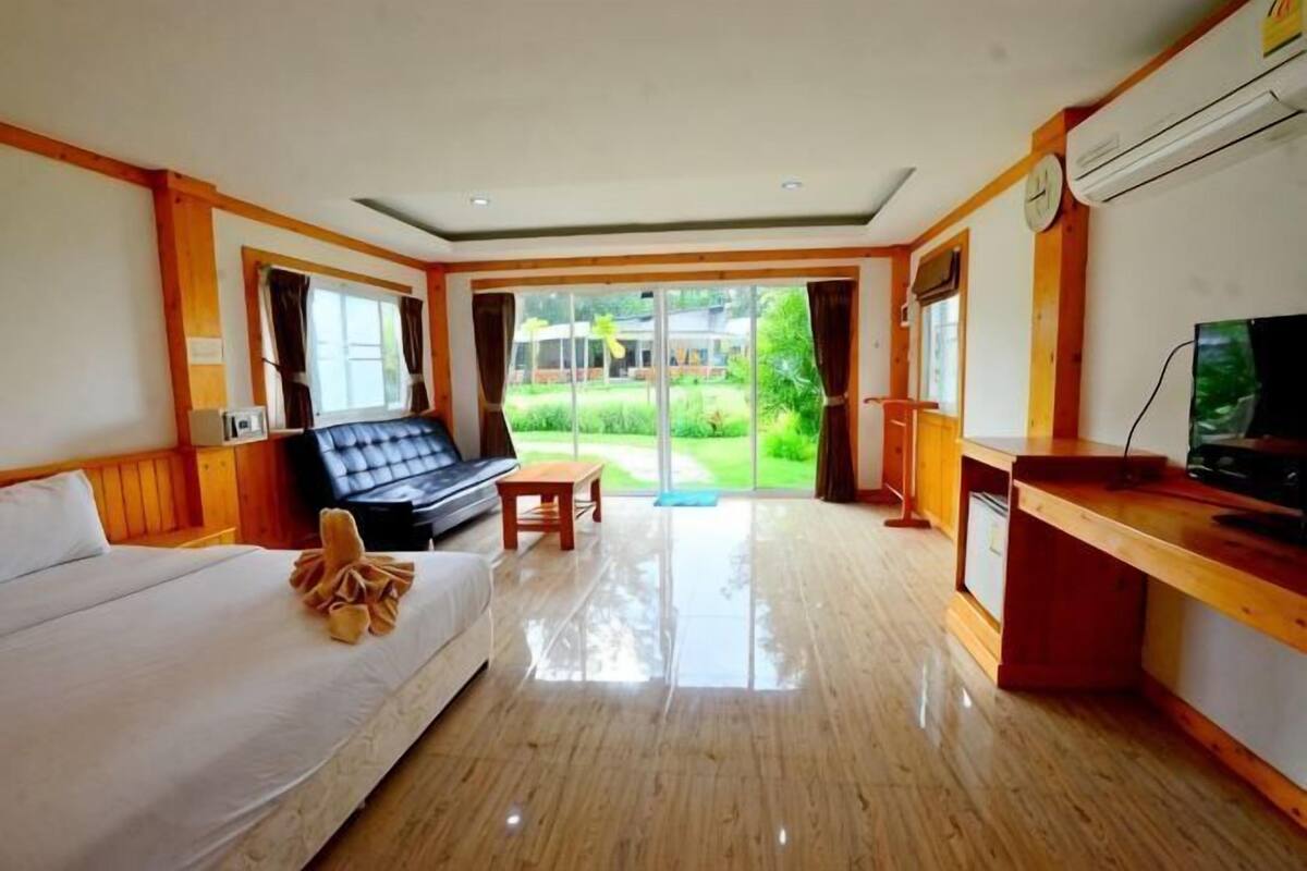 Quarto de hotel com cama, sofá, televisão, escrivaninha e vista para um jardim.