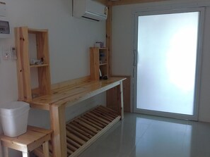 A room with a wooden desk, a white trash bin, a wooden shelf unit, and a sliding glass door.