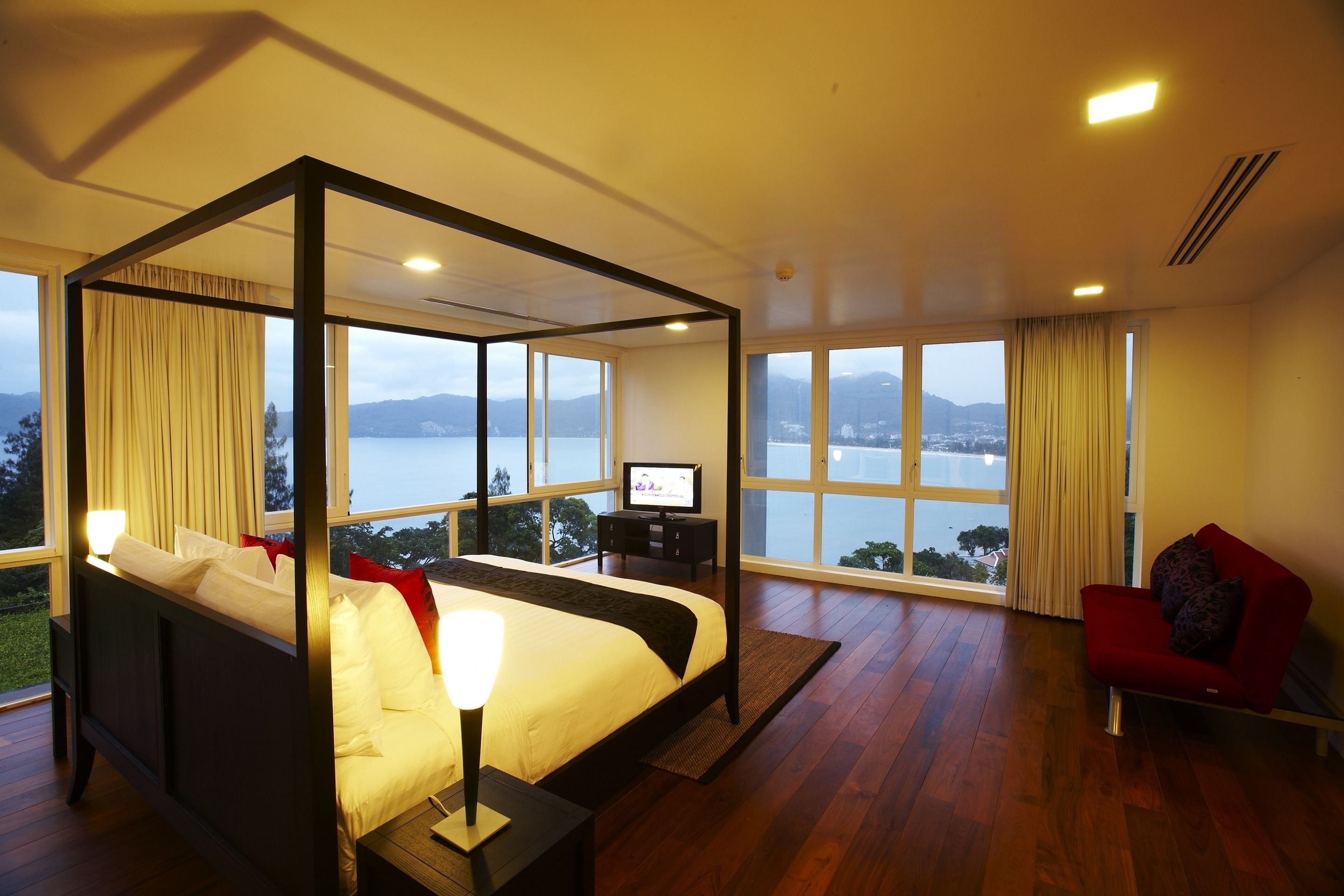 A spacious bedroom with a four-poster bed, a television, and a red armchair.