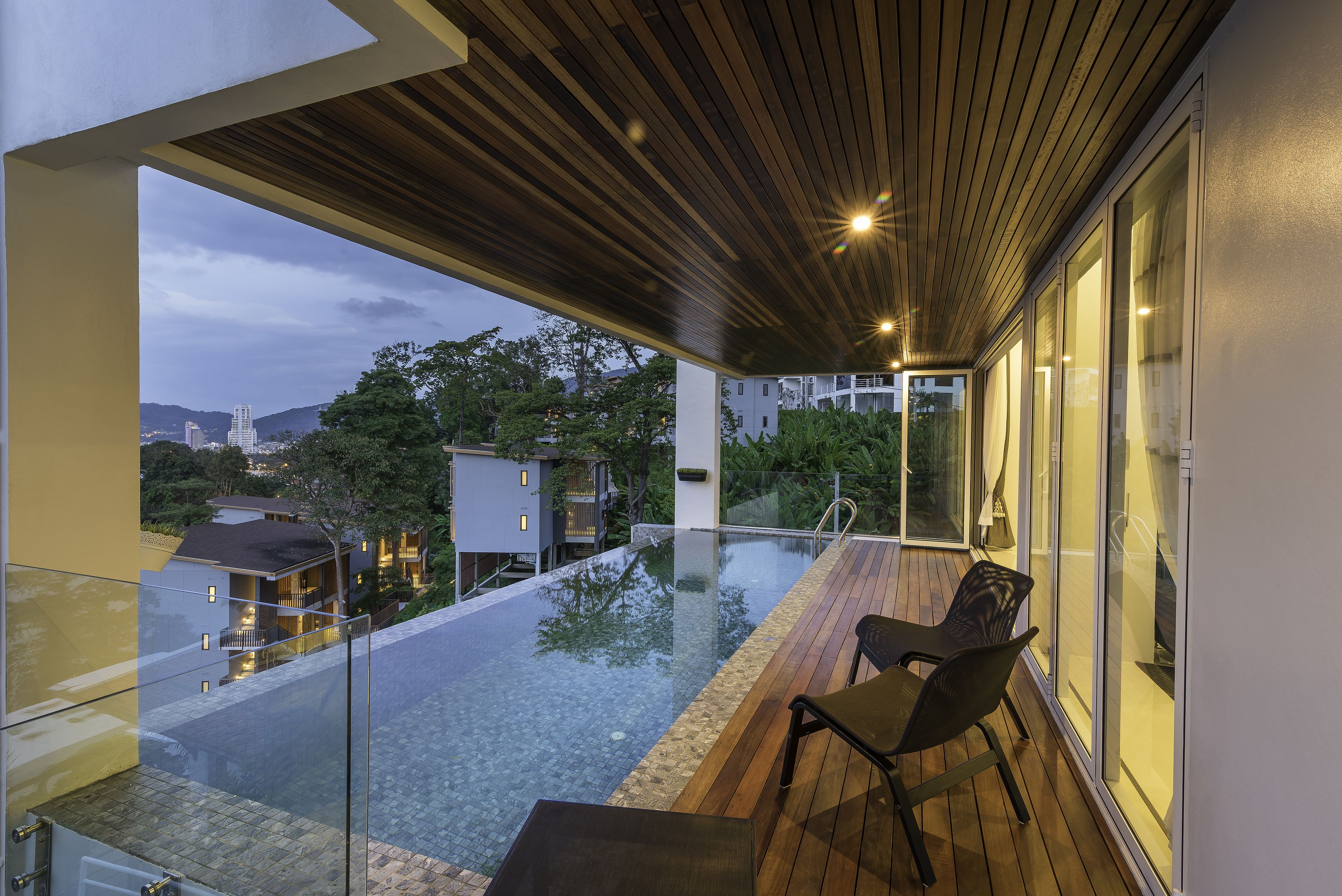 A modern outdoor balcony with a glass barrier, wooden flooring, and a chair.
