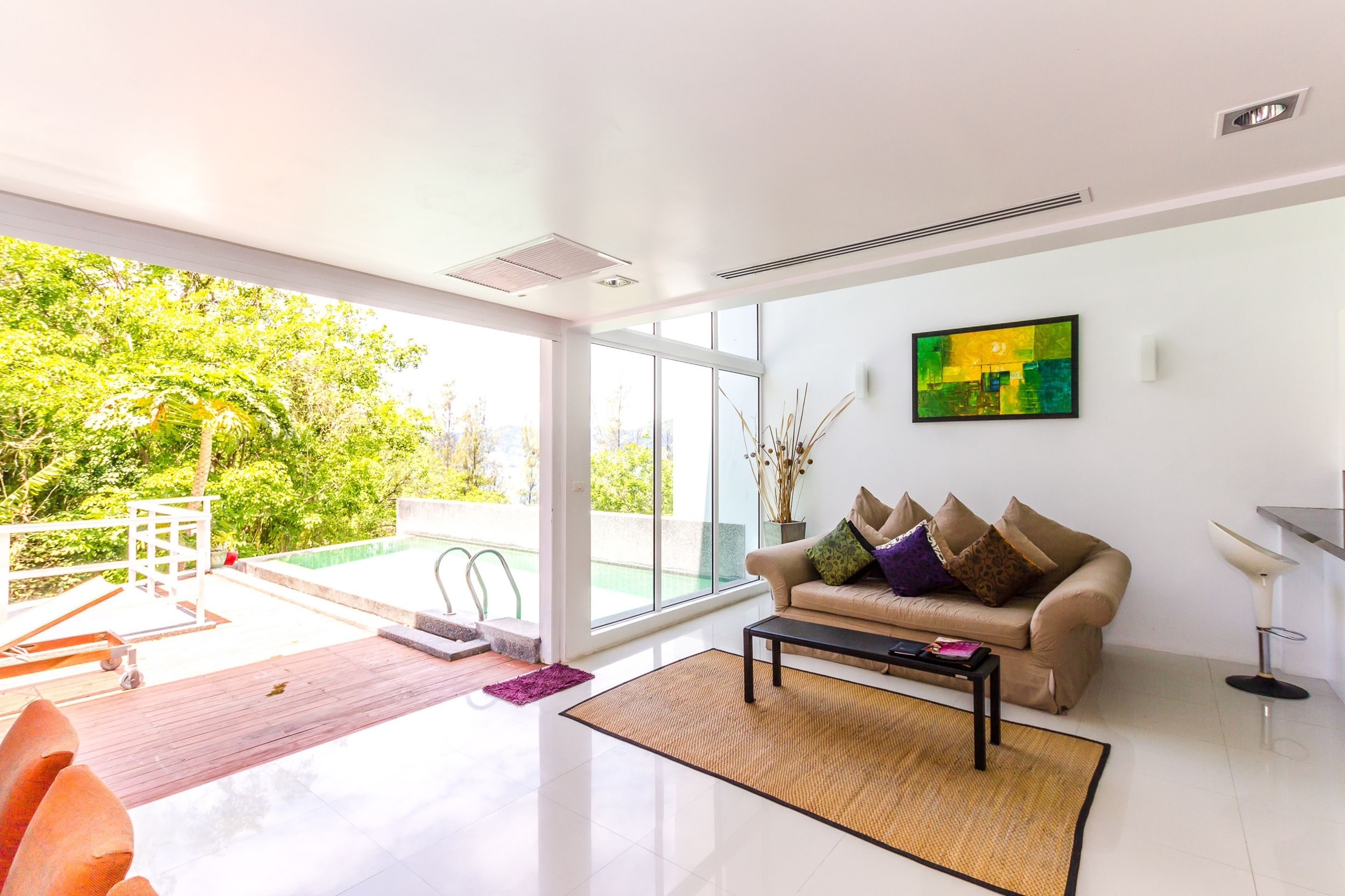 A modern living room with a sofa, coffee table, and a large window offering a view of greenery outside.