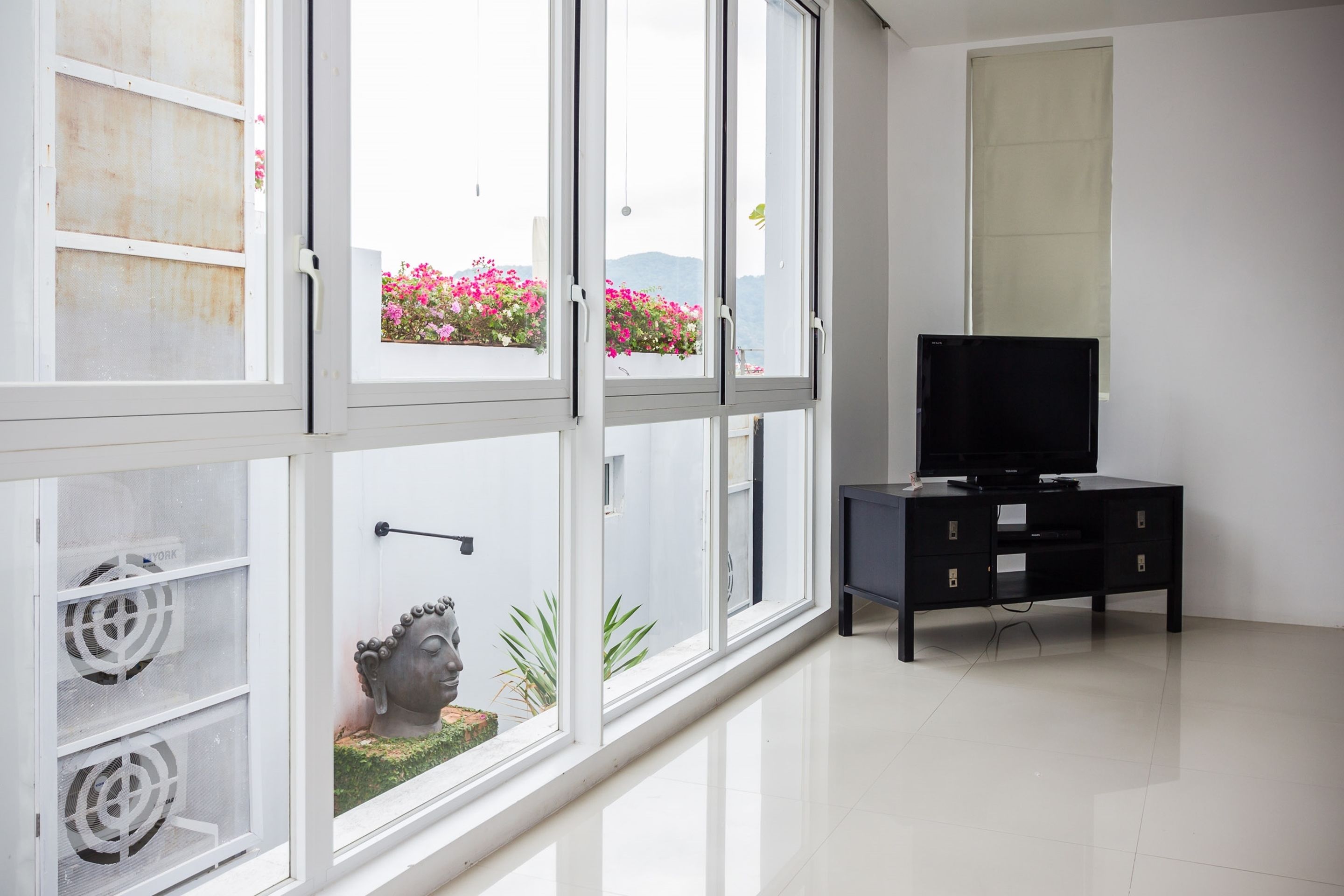 A modern living room with a large window, a black entertainment unit, and a Buddha statue.