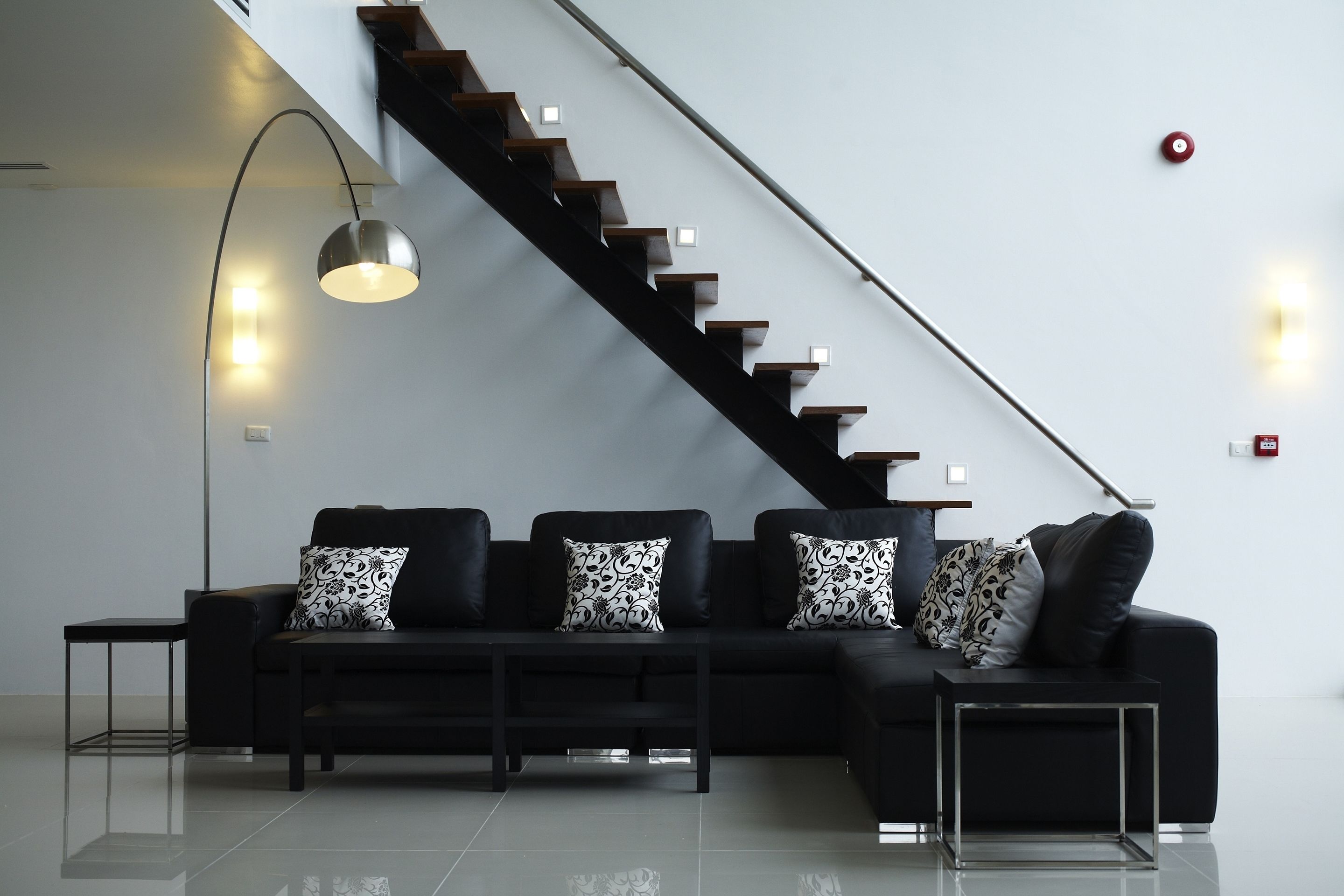 Een moderne woonkamer met een zwarte bank, decoratieve kussens, een salontafel en een trap met een leuning.