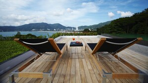 A wooden deck with two lounge chairs and a table, overlooking a body of water and mountains. - Jirana Patong (Patong)