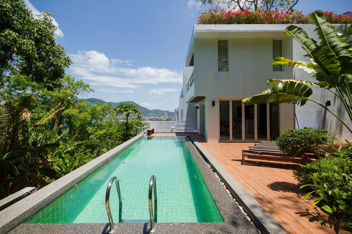 A modern pool area with a clear view of the mountains in the background, surrounded by lush greenery.