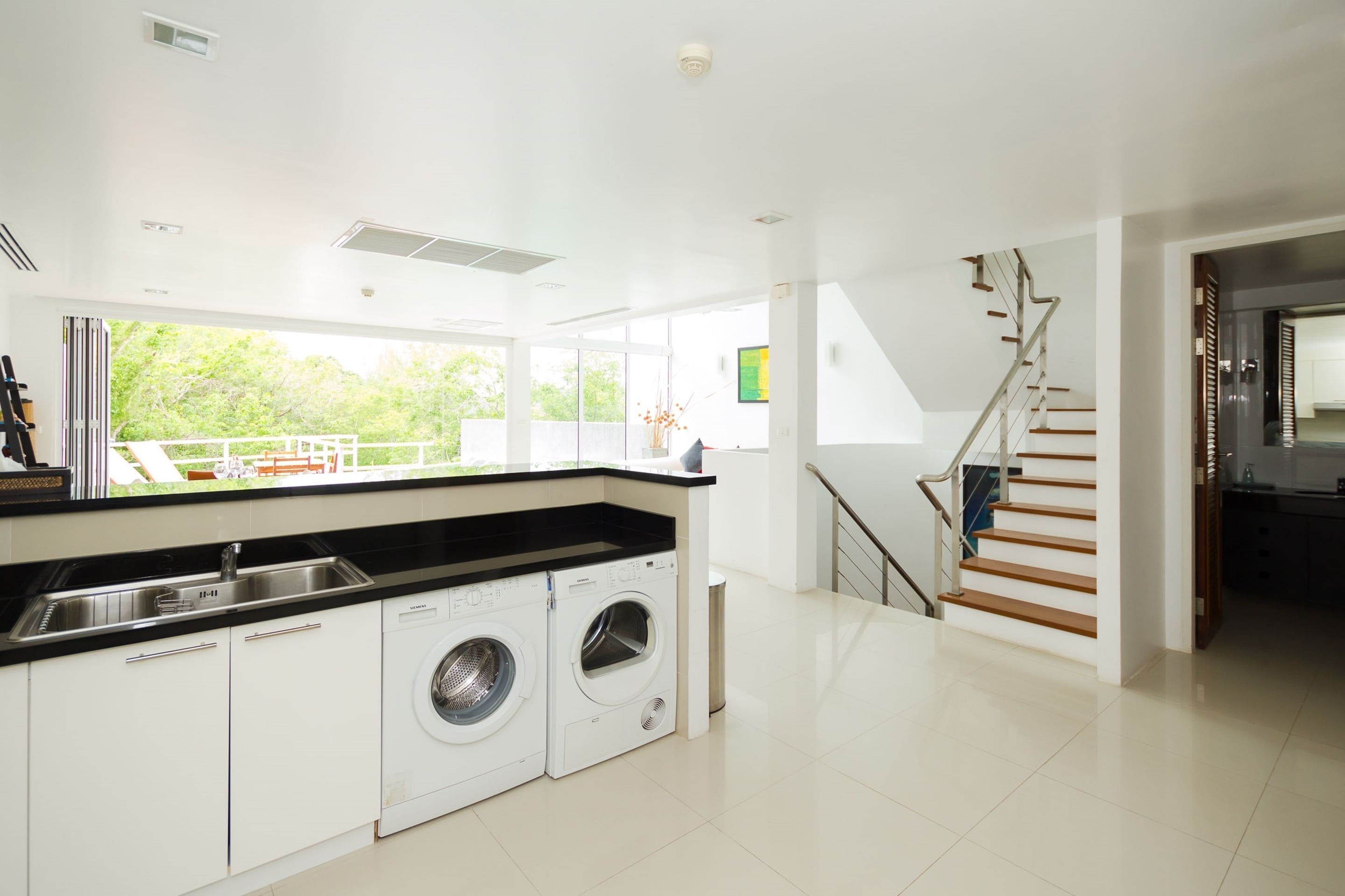 Een moderne keuken met inbouwapparatuur, een groot raam en een trap.