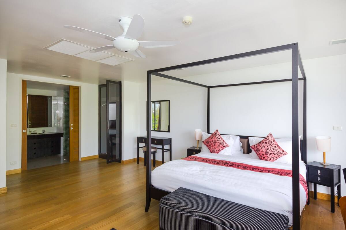 A four-poster bed with a canopy, a desk with a chair, a mirror, and a nightstand with a lamp.