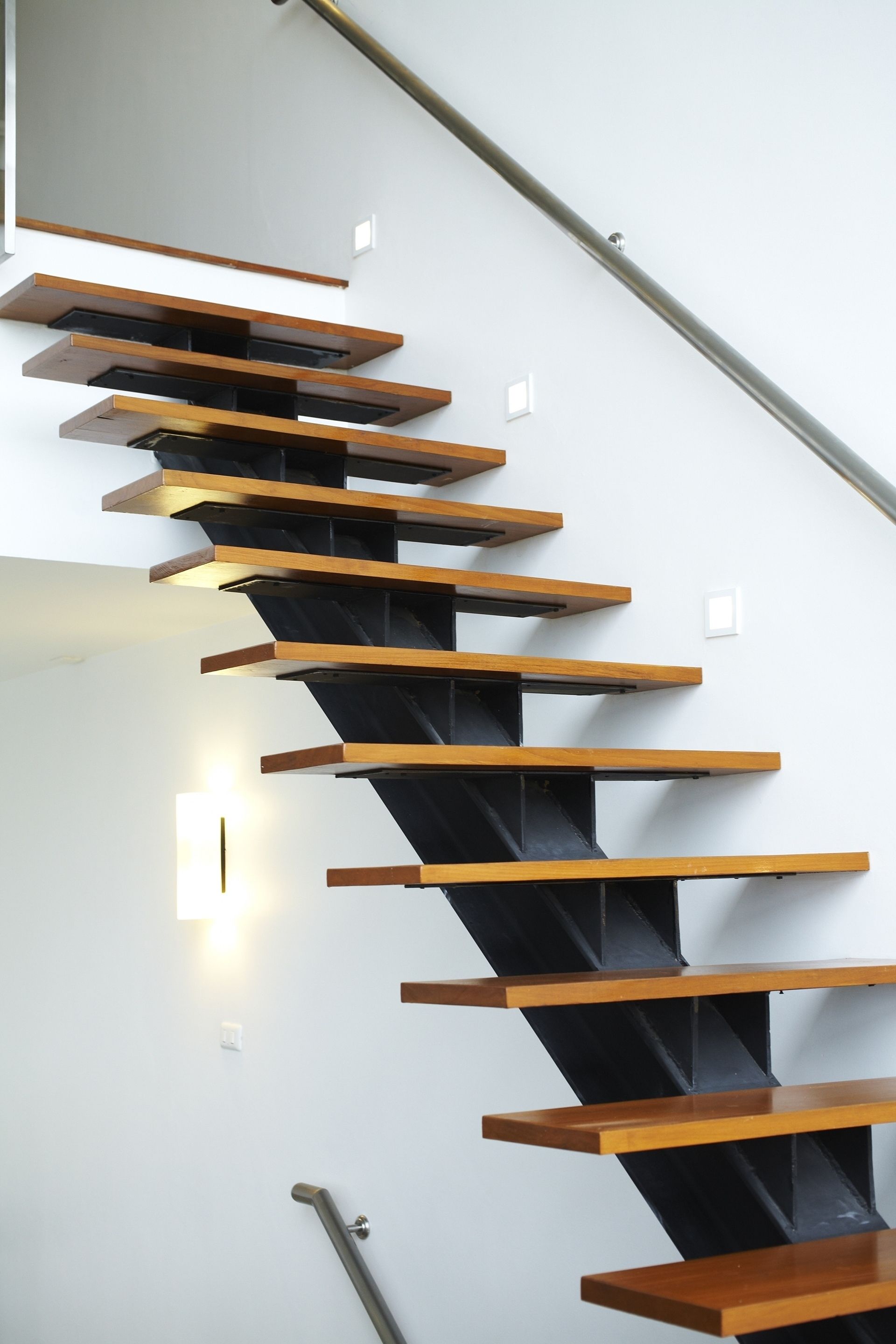 Una moderna scala con gradini in legno e ringhiere nere, che conduce a un piano superiore.
