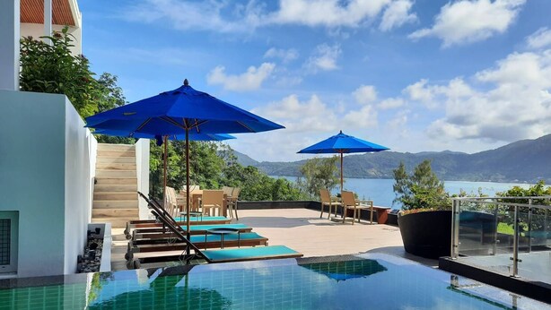 A pool area with blue umbrellas, a view of mountains, and a clear sky. - Jirana Patong (Patong)