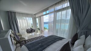 A modern bedroom with a large bed, a seating area with a sofa and chairs, and a balcony with a view of the sea. - Jirana Patong (Patong)