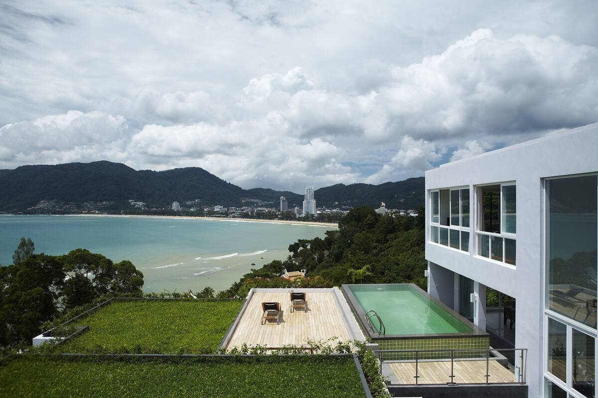 A modern building with a rooftop pool and a view of a beach and mountains.