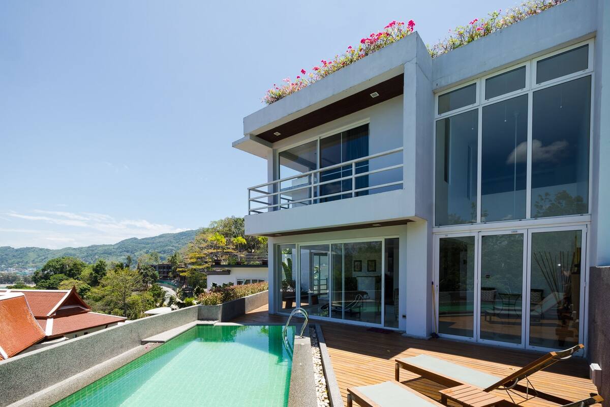 A modern two-story house with a swimming pool, wooden deck, and a balcony with flowers.