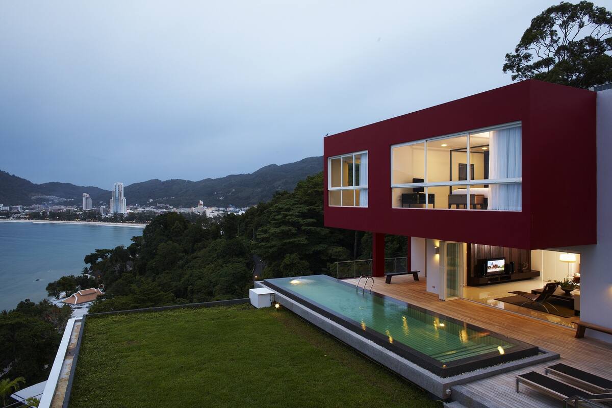 A modern house with a pool, large windows, and a view of the sea and mountains.