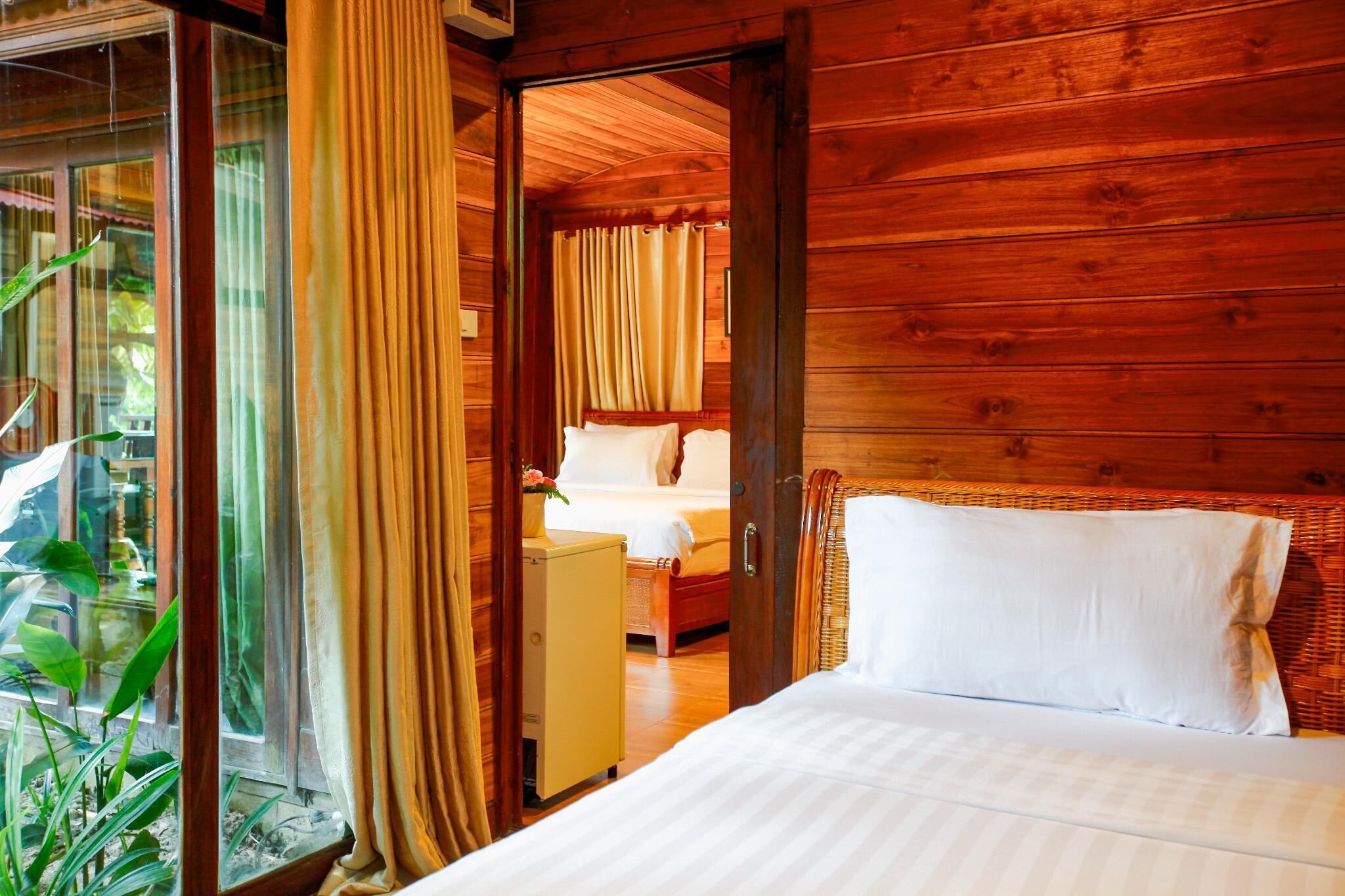 Una habitación de madera con una cama, un armario pequeño y un vidrio que da a otra habitación.