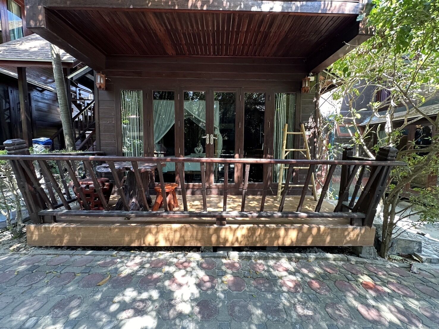 A wooden deck with a railing, a ladder, and a staircase leading to a covered area with a view of the surrounding buildings.