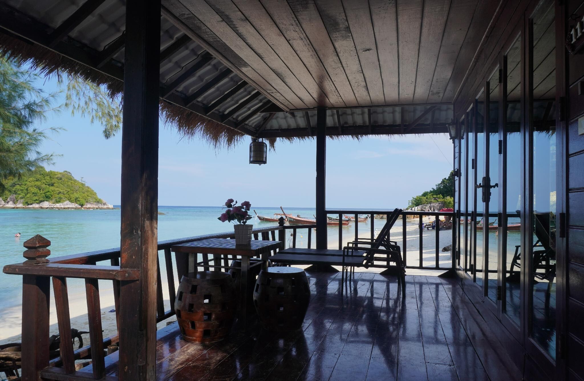 A wooden deck with a thatched roof overlooking a beach.