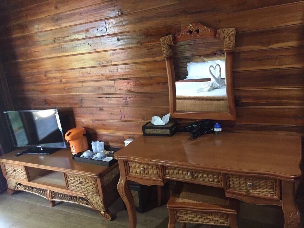 A wooden room with a TV on a wooden cabinet, a mirror with a heart design, and a wicker chair.