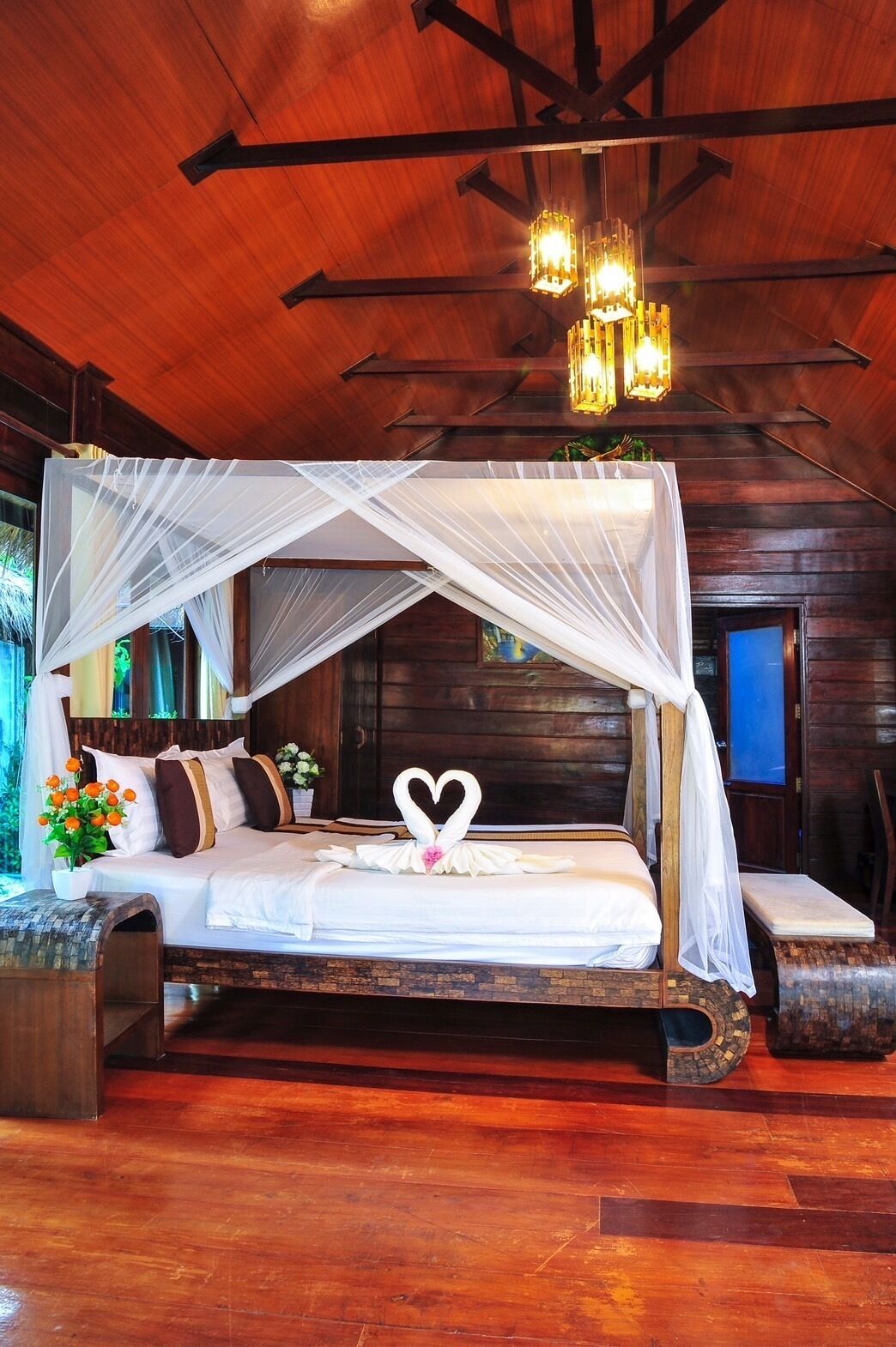 A wooden cabin-style bedroom with a canopy bed, a bench, and a small table with flowers.