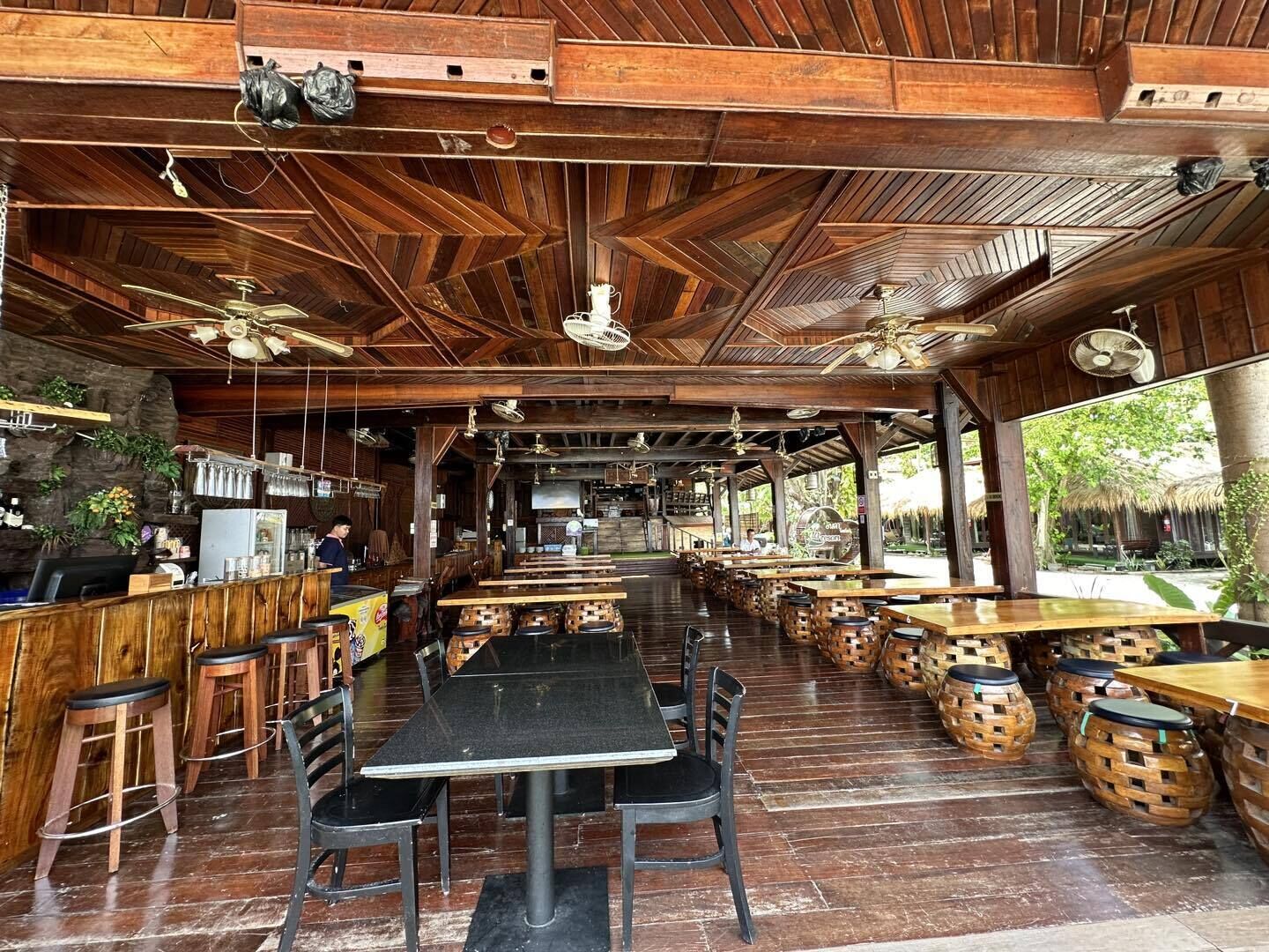 A restaurant with wooden interiors, multiple tables and chairs, and ceiling fans.