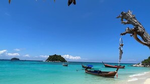 A beach with clear turquoise water, several boats, and a small island in the distance. - Anda Resort Koh Lipe (Koh Lipe)