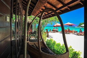 A beachside view with a thatched roof structure, wicker chairs, and a sandy beach with umbrellas.