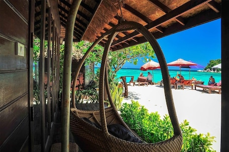 A beachside view with a thatched roof structure, wicker chairs, and a sandy beach with umbrellas.