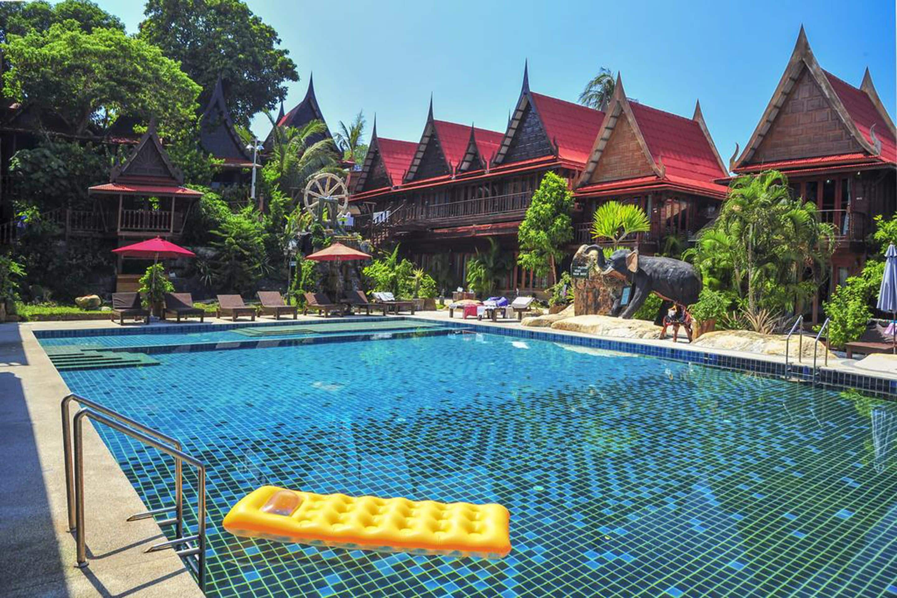 A swimming pool with a wooden deck, lounge chairs, and a water wheel.