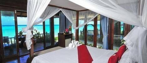Un dormitorio con una cama grande, cortinas blancas y vistas al océano.