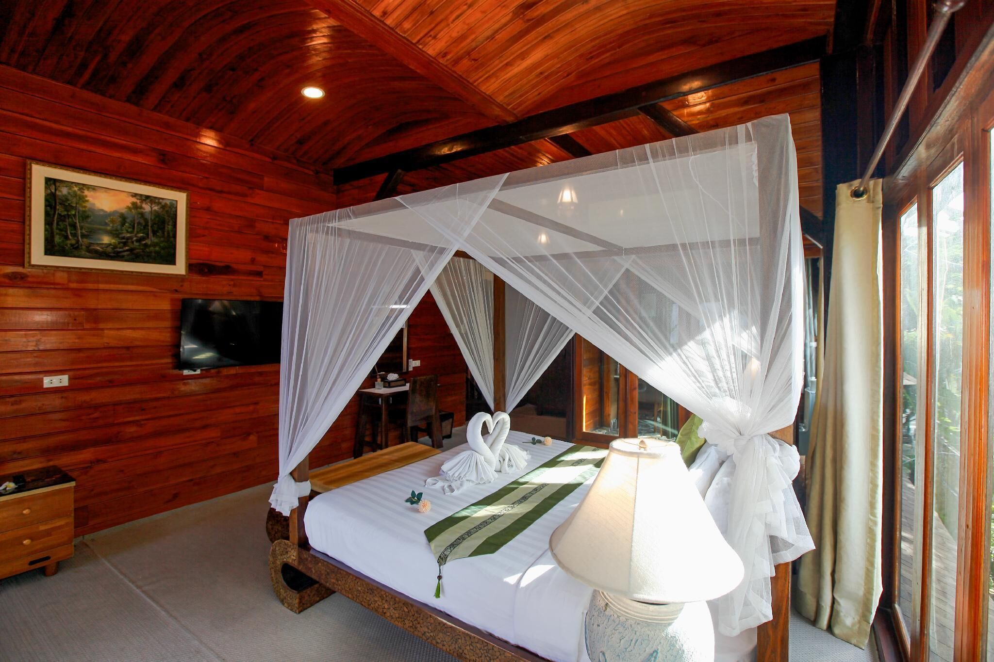 A wooden cabin bedroom with a bed, canopy, bedside lamp, and a painting on the wall.