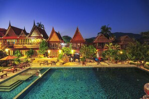 A resort with traditional architecture, a swimming pool, and outdoor seating areas.
