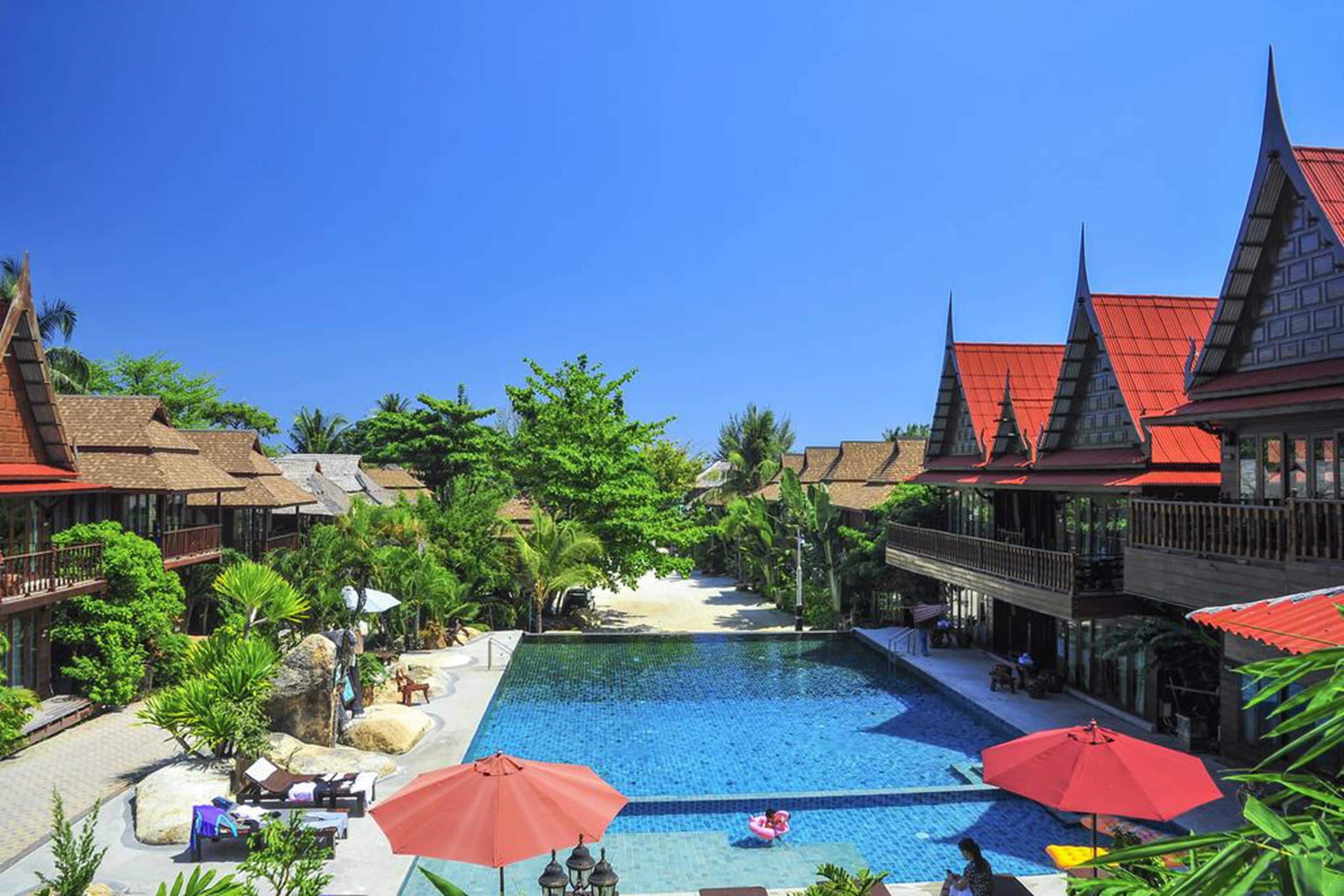 Un resort con piscina rodeada de arquitectura tradicional, palmeras y zonas de estar al aire libre.