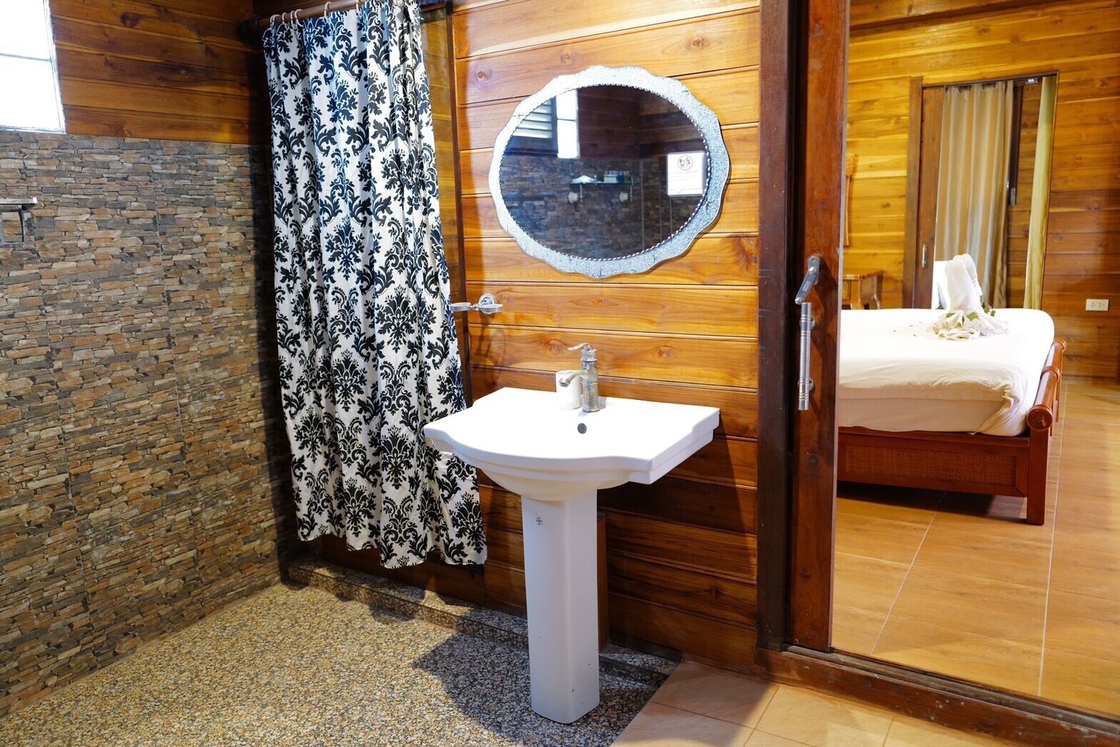 A bathroom with a stone wall, a white sink, a mirror, and a bed with a white bedspread.