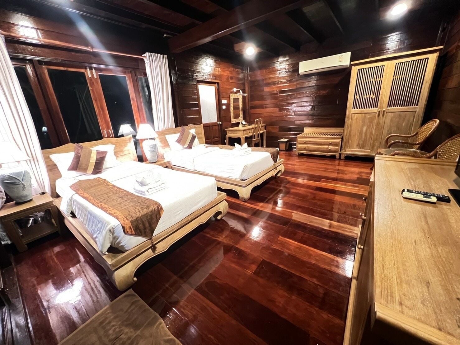 A hotel room with two wooden beds, a wooden wardrobe, a wooden desk, and a wooden chair.