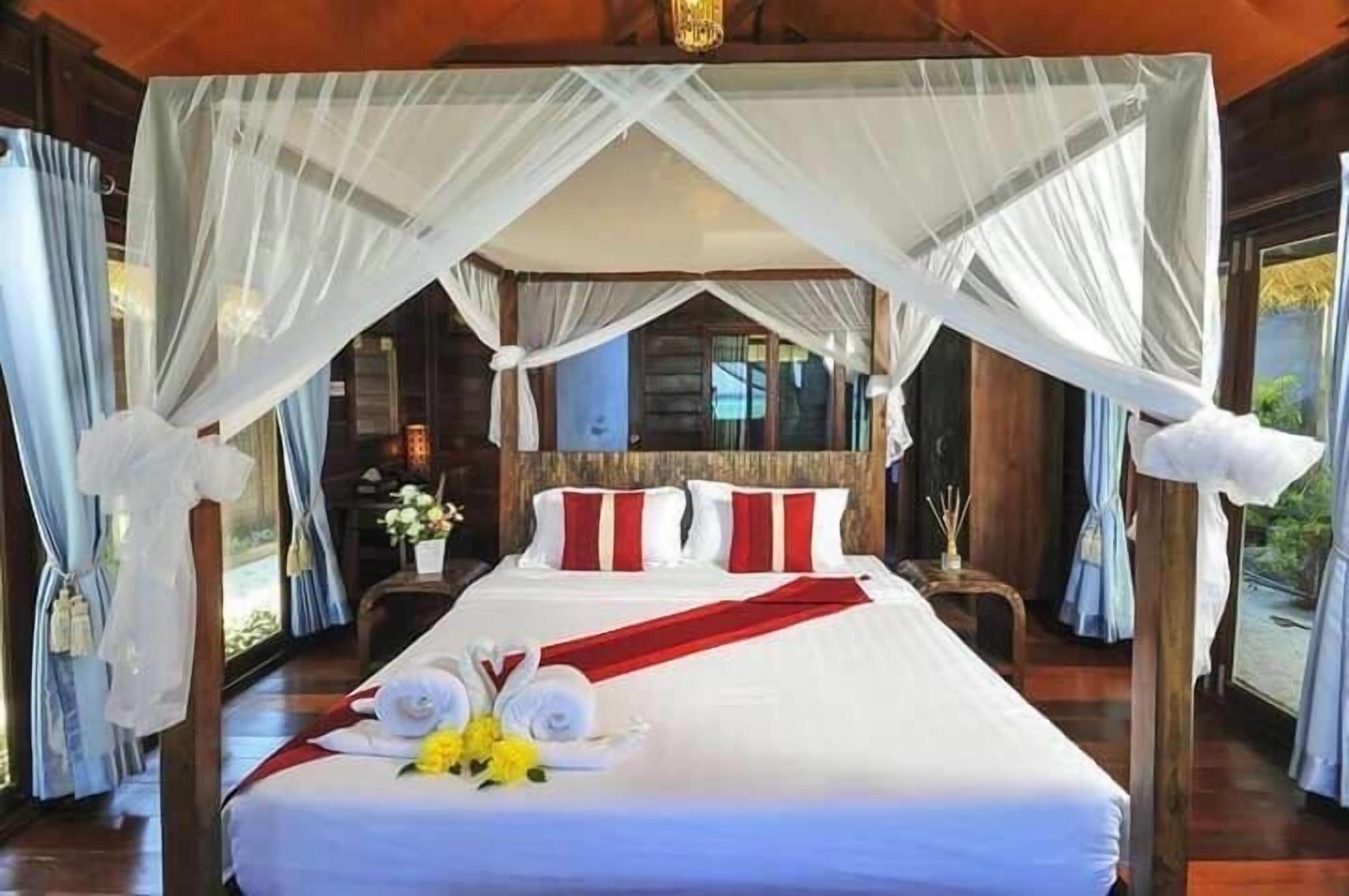 A bed with white linens and red accents, a canopy, and a bouquet of flowers.