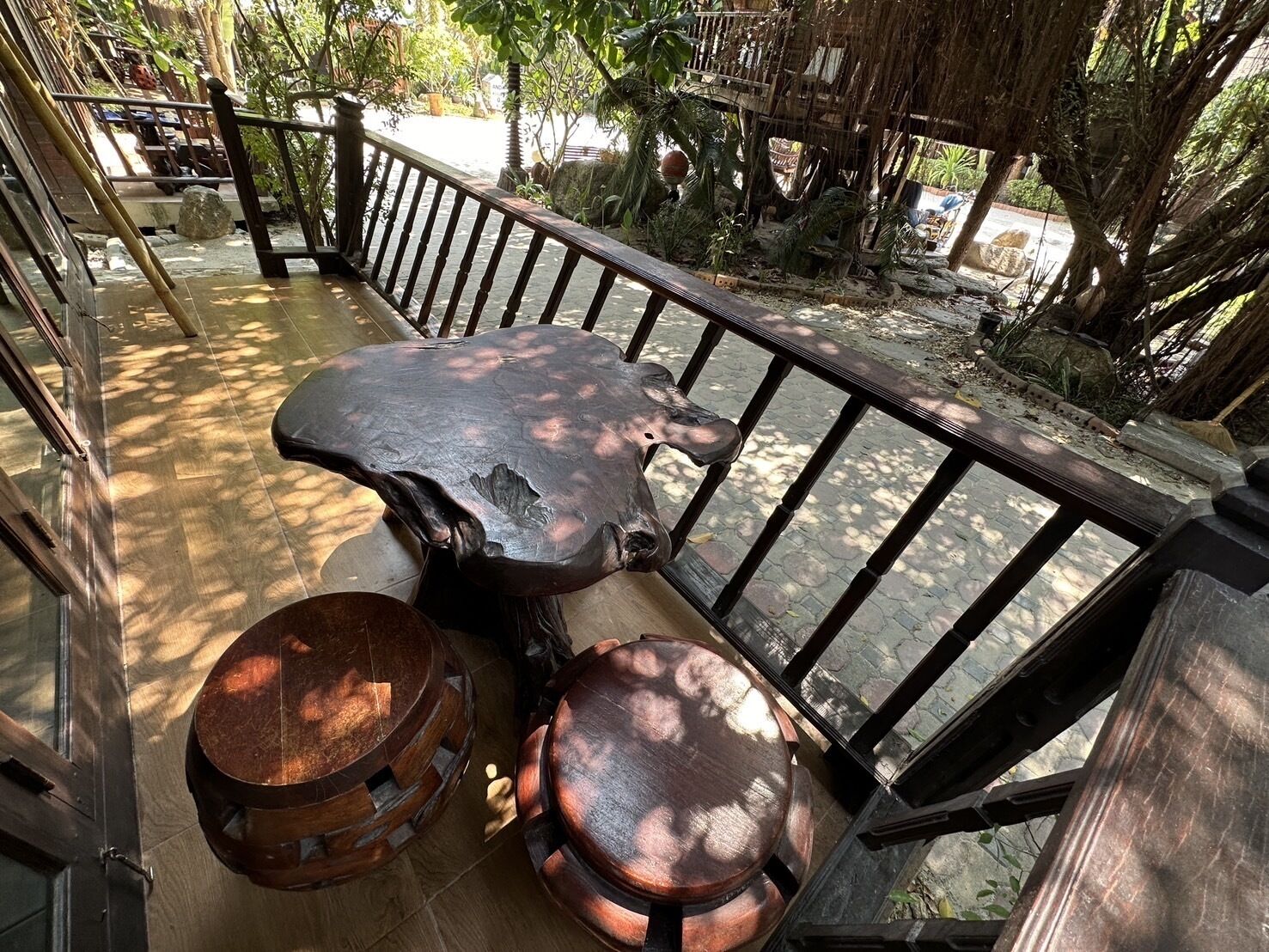 A wooden deck with a rustic bench and two round stools, surrounded by a wooden railing and lush greenery.