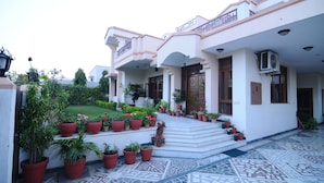 A building with a white facade, multiple balconies, and a tiled entrance area with potted plants. - Jaipur Friendly Villa (Jaipur)