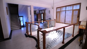 A spacious interior with a staircase leading to a balcony, a large window with a view, and a ceiling fan. - Jaipur Friendly Villa (Jaipur)