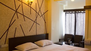 Una habitación de hotel con una cama grande, dos almohadas, una mesita de noche con una lámpara, una silla y una ventana con cortinas.