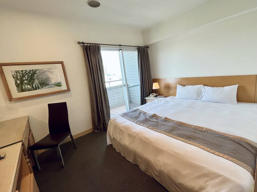 Una habitación de hotel con una cama grande, un escritorio con silla, un cuadro en la pared y una ventana con cortinas.
