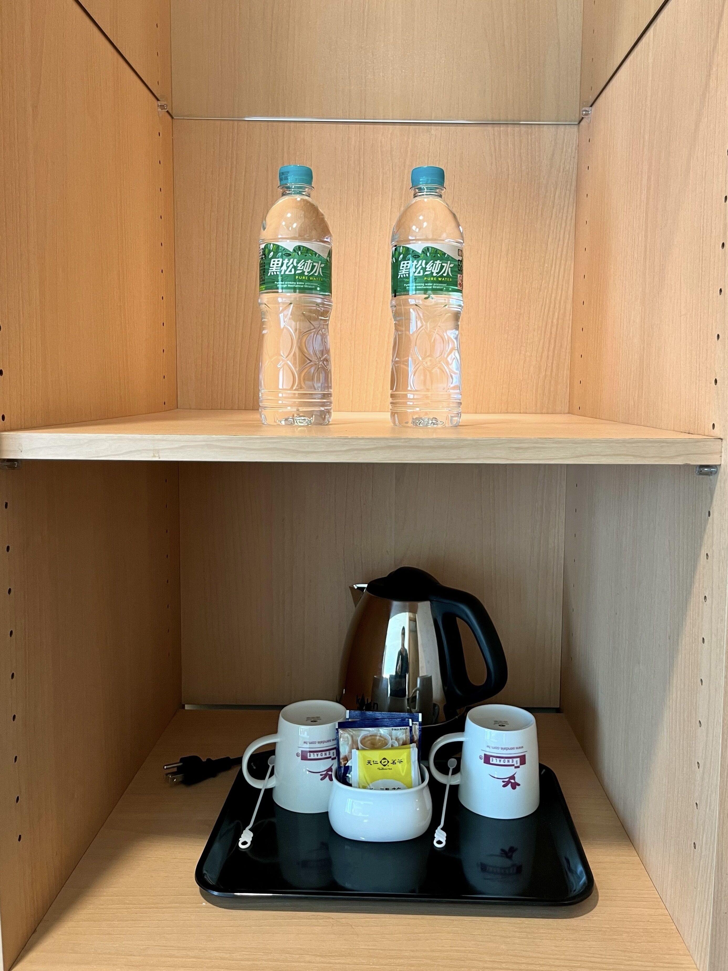 A wooden shelf with two water bottles and a tray with cups and a kettle.