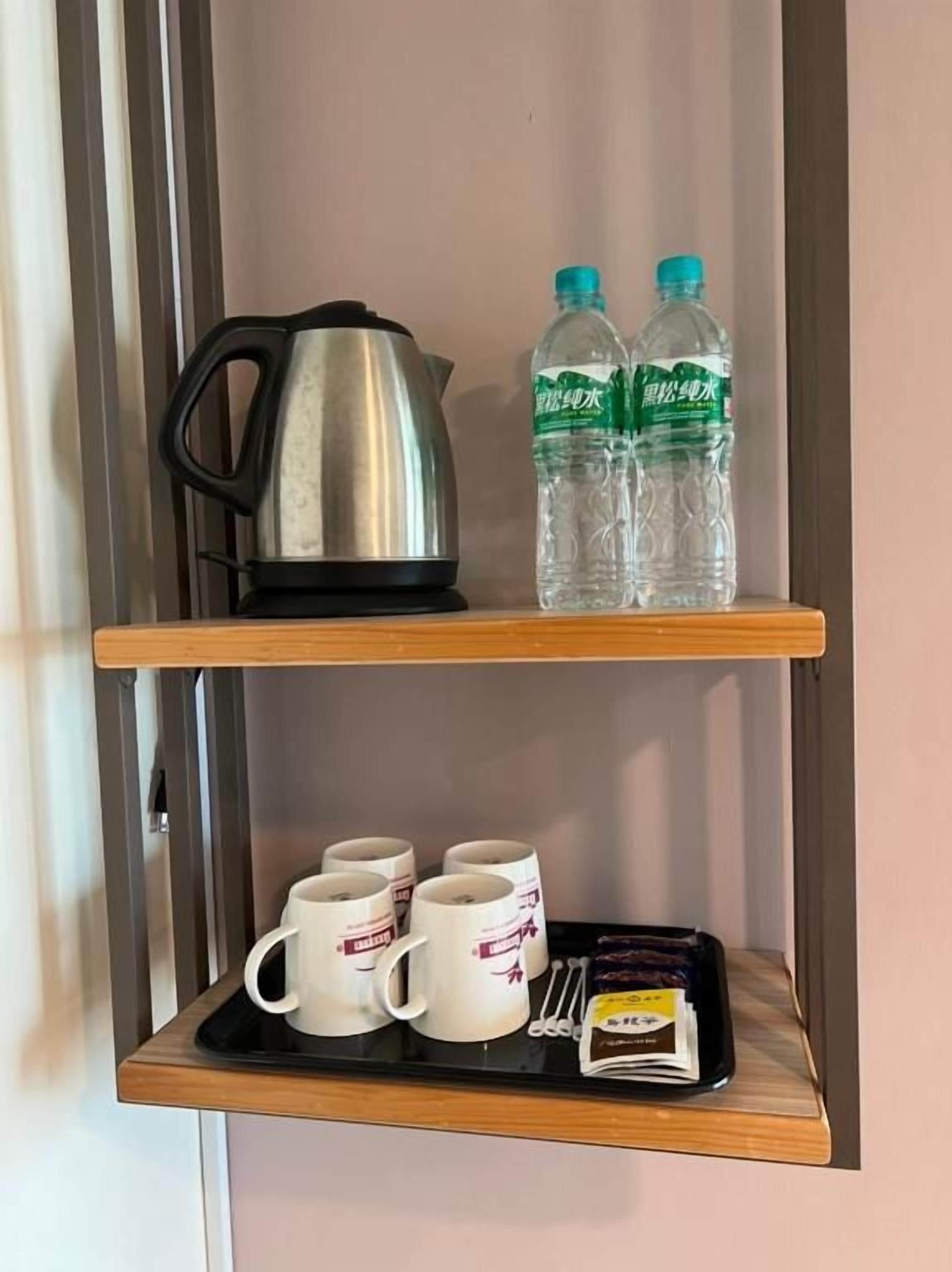Une étagère avec une bouilloire, deux bouteilles d’eau et un plateau contenant des tasses et une boîte de thé.