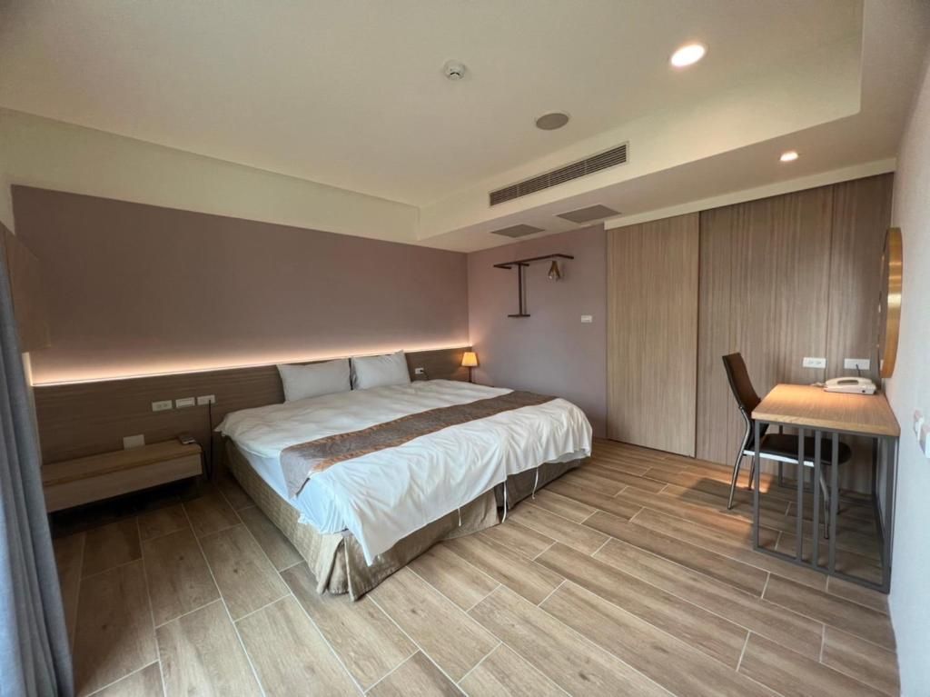 A modern hotel room with a large bed, bedside table, and a desk with a chair.
