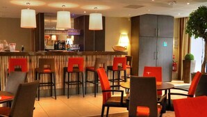 Eine moderne Hotelhalle mit Barbereich, roten und braunen Sesseln und einer großen Topfpflanze.