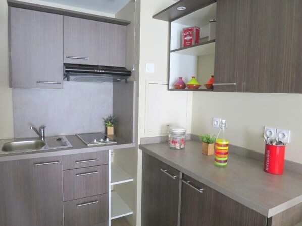 A modern kitchen with grey cabinets, a stainless steel sink, and a countertop with a red utensil holder and a striped container.
