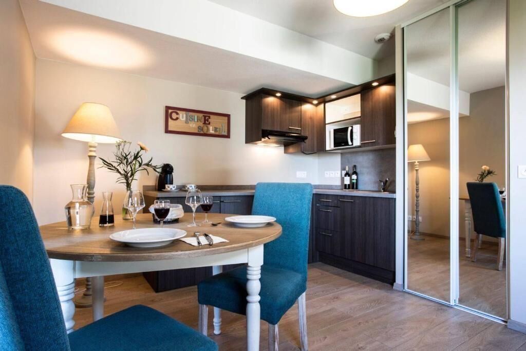 A modern kitchen with dark cabinetry, a microwave, and a dining area with a round table and blue chairs.