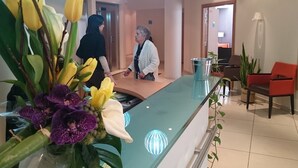 Ein Empfangsschalter mit Glasplatte, ein Blumentopf mit gelb und violett blühenden Pflanzen und ein roter Stuhl im Hintergrund.