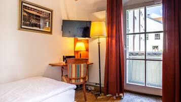 Una habitación con techo de madera, una cama, un escritorio con lámpara, una silla y una ventana con cortinas.
