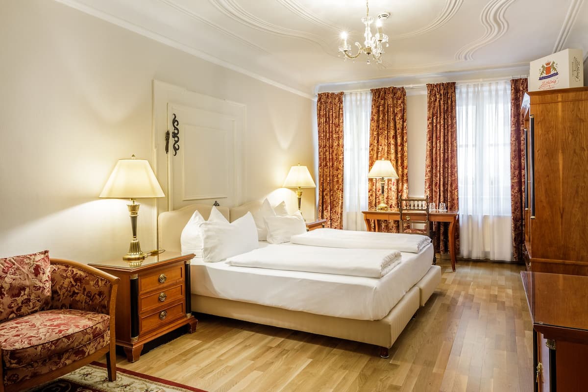 Habitació d'hotel amb un llit gran, una taula de treball, una cadira, un sofà i una catifa vermella amb dibuixos.