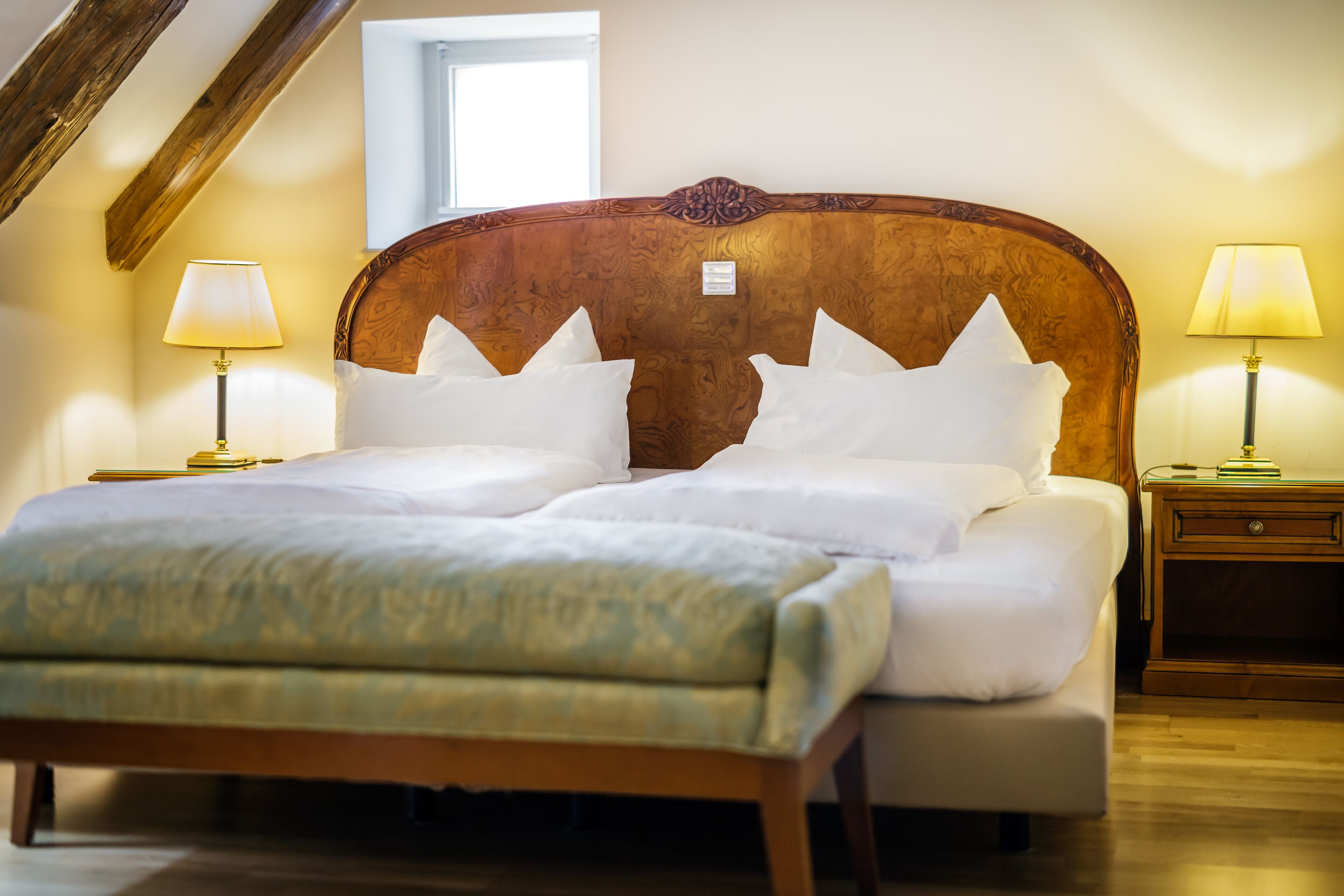 A neatly made bed with white linens and pillows, two bedside tables with lamps, and a wooden headboard.