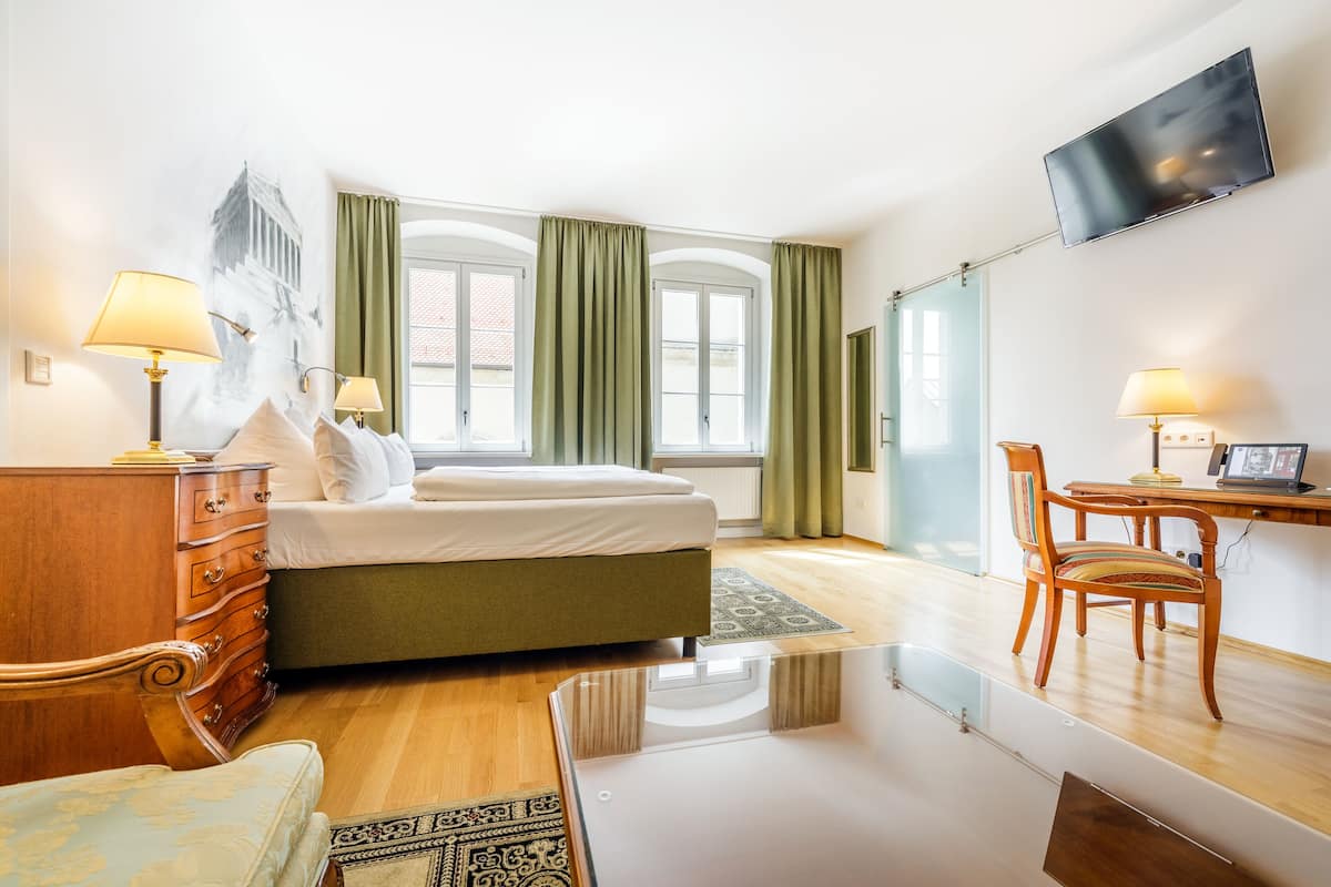 Habitació d'hotel amb llit, escriptori, cadira, televisió i finestra amb cortines.